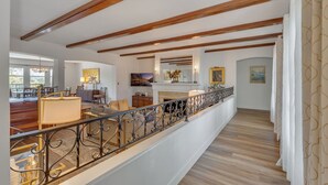 Amplia sala de estar con techo alto, vigas de madera, balcón con barandilla de hierro forjado y vistas al exterior.
