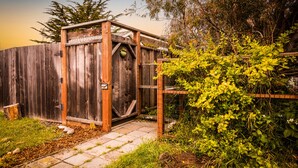 A wooden structure with a door, surrounded by greenery and a fence.