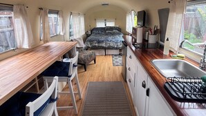 A compact RV interior with a kitchenette, a dining area, and a sleeping space.
