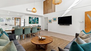 A modern living room with a dining area, a flat-screen TV mounted on the wall, and a large abstract painting. - Fuller Holidays - Somerset@Byron (Byron Bay)