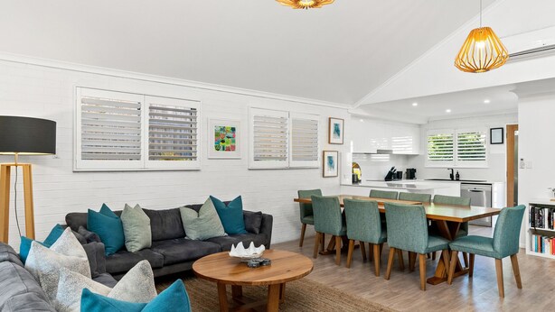 A modern living room with a sofa, coffee table, and dining area. - Fuller Holidays - Somerset@Byron (Byron Bay)