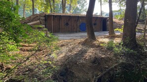 Een rustieke houten hut met een rond raam, omgeven door dicht bos.
