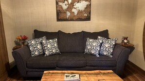 Een woonkamer met een donkergrijze bank, gestreepte kussens, een houten salontafel en een wereldkaart aan de muur.