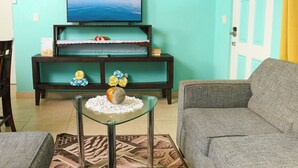 A living room with a television on a stand, a sofa, a glass coffee table, and a patterned rug.