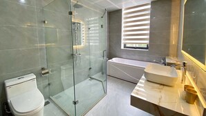 A modern bathroom with a glass-enclosed shower, a standalone toilet, a freestanding bathtub, and a vanity with a large mirror. - Daily Hotel (Bai Chay)