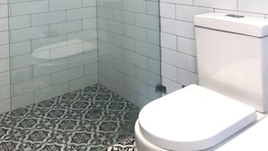 A bathroom with white subway tiles, a glass shower enclosure, a toilet, and patterned floor tiles. - Story Bank Mandurama   (Mandurama)