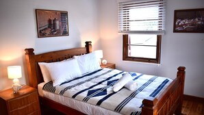 A neatly made bed with a striped blanket, wooden headboard, and two bedside tables with lamps. - Story Bank Mandurama   (Mandurama)