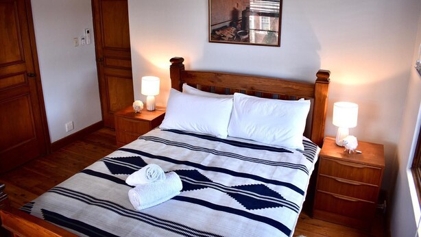 A neatly made bed with a striped blanket, two bedside lamps, and a painting on the wall. - Story Bank Mandurama   (Mandurama)