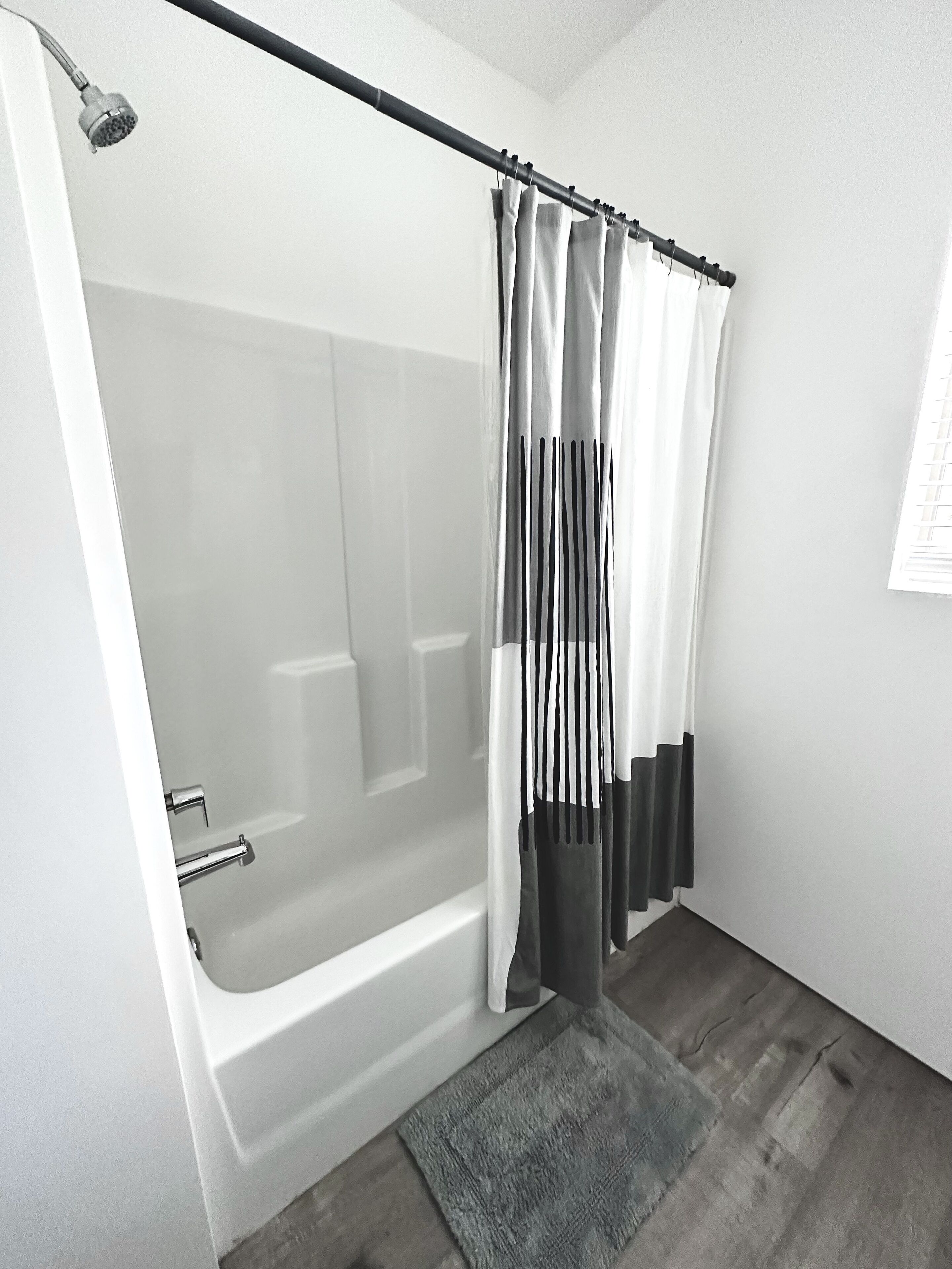 Une salle de bain moderne avec une douche à l’italienne, une baignoire blanche et un tapis gris.