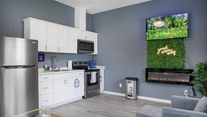 A modern kitchen with white cabinets, stainless steel appliances, and a flat-screen TV mounted on a green wall. - Modern Mid-Town Luxury Hideaway  (Savannah)