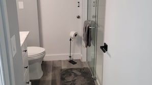 Een moderne badkamer met toilet, een douchecabine van glas en een witte wastafel.