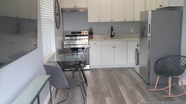 Een moderne keuken met witte kasten, een roestvrijstalen koelkast, een inbouwoven en een glazen eettafel met stoelen.