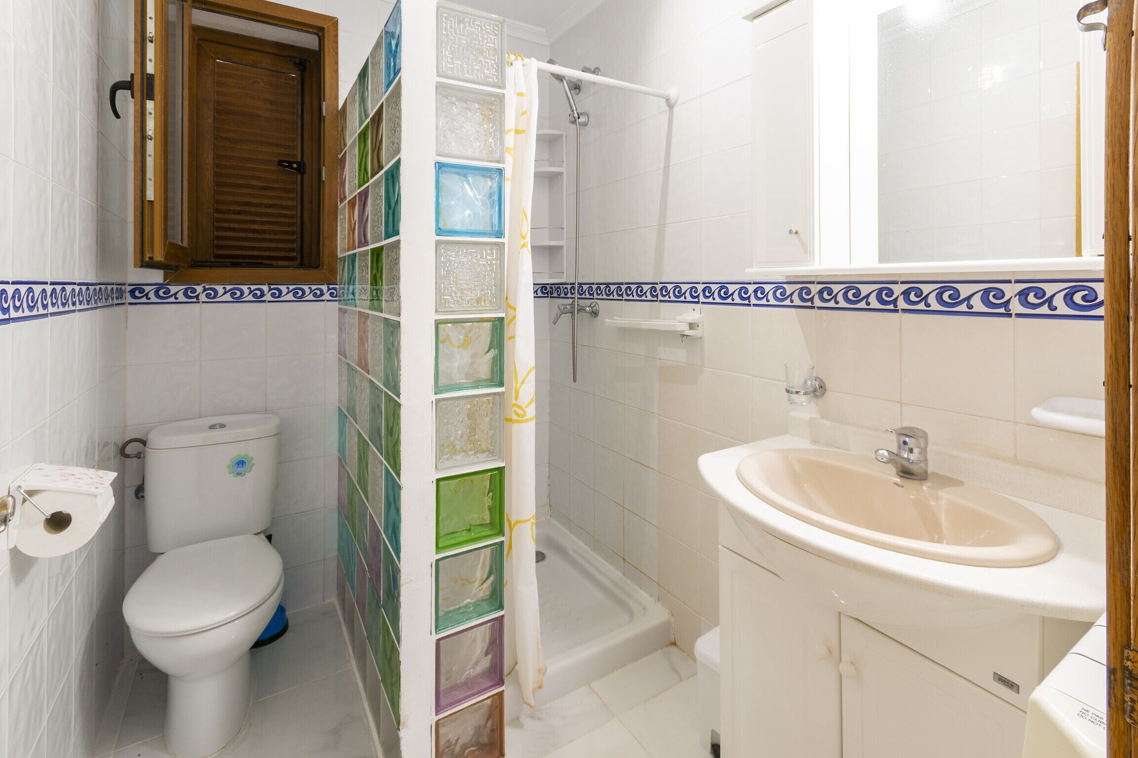 Un baño con inodoro, ducha, lavabo y pared de azulejos con un borde decorativo.