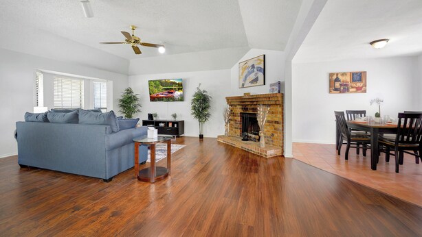 A spacious living room with hardwood flooring, a blue sofa, a fireplace, and a dining area with chairs and a table. - Spacious 2BR home near Downtown Dallas and State Fair of Texas (Dallas)