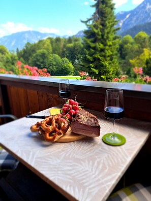 A table with pretzels, a loaf of bread, and two glasses of red wine on a balcony with a mountain view. - Ferienwohnung Bergstüberl mit Südbalkon, 1-3 Personen, 50 qm (Bad Reichenhall)
