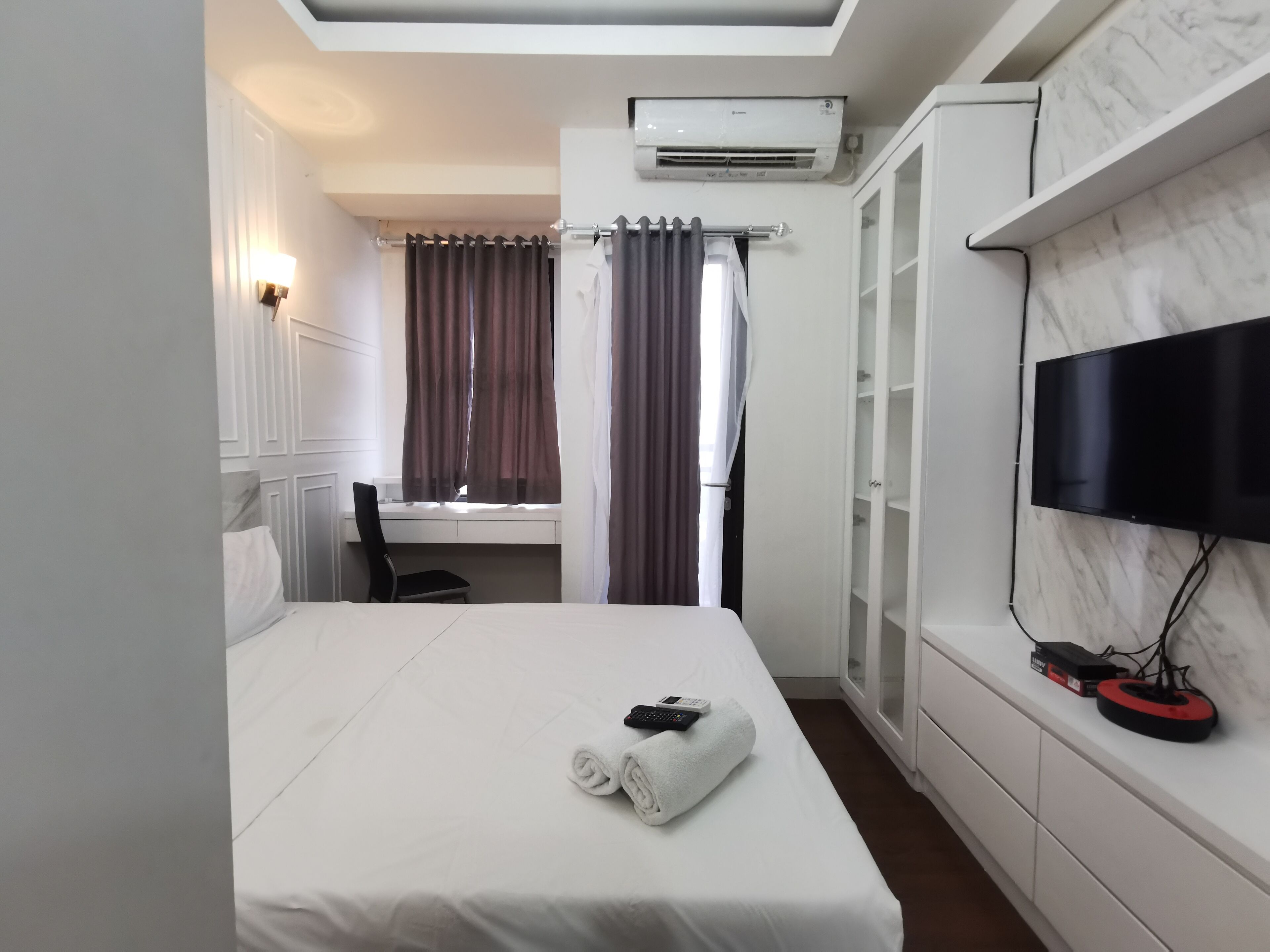 A hotel room with a bed, a desk, a chair, a TV, and a wardrobe.