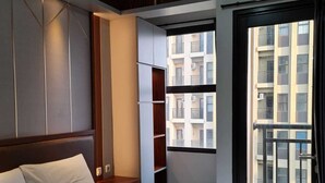 A hotel room with a large bed, built-in wardrobe, and a view of a residential building through a window. - ARSAKHA 003 Transpark cibubur By Karlina (Depok)