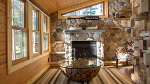 A cozy cabin interior with a stone fireplace, wooden walls, and a glass coffee table. - Newly Remodeled Lakefront Cabin w/ Modern Amenities. (Traverse City)