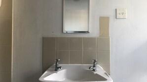 Een badkamer met een wit wastafel, twee kraan, een spiegel en een lichtschakelaar.