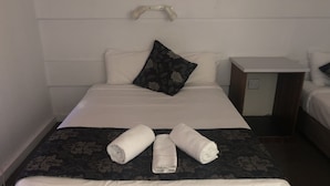 Een netjes opgemaakt bed met witte linnens, een bloemenprintdeken en twee opgerolde handdoeken op het bed.