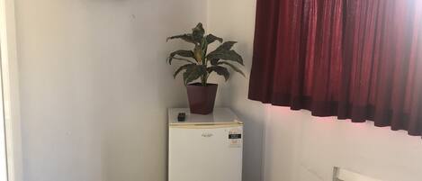 Una habitación compacta con un refrigerador blanco, una planta en maceta, un televisor de pantalla plana y una cortina roja.