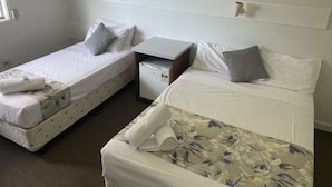 Twee enkele bedden met witte lakens en een bloemrijk sprei, een klein wit bureau en een witte muur met een deur.