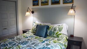 A neatly made bed with floral bedding, two bedside lamps, a nightstand with a clock, and a door to the left.