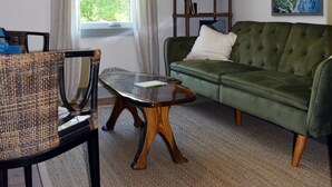 A living room with a green sofa, a wooden coffee table, a wicker chair, a bookshelf, and a ceiling fan.