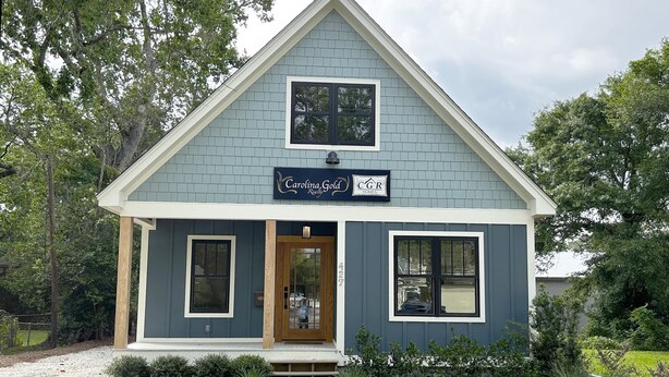 A two-story house with a dark blue exterior, a front porch, and a sign that reads "Carolina Gold CGR Homes."