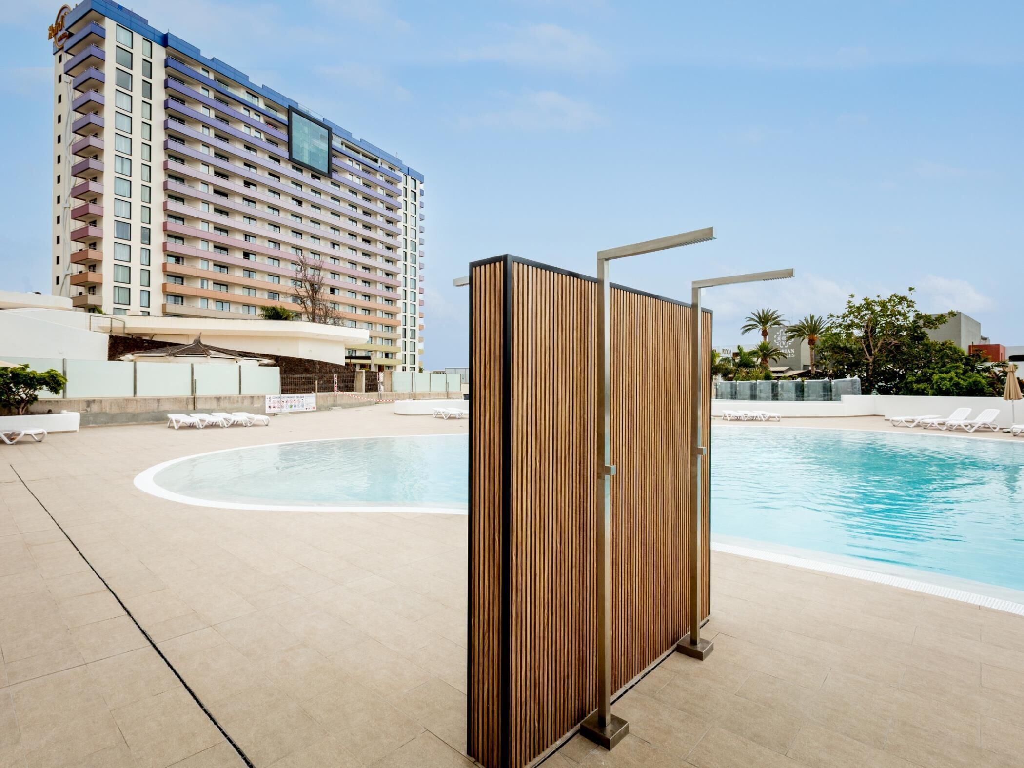 A hotel pool area with a large pool, lounge chairs, and a tall building in the background.