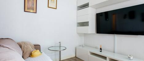 A modern bedroom with a bed, a small round table, a TV mounted on the wall, and a white console unit.