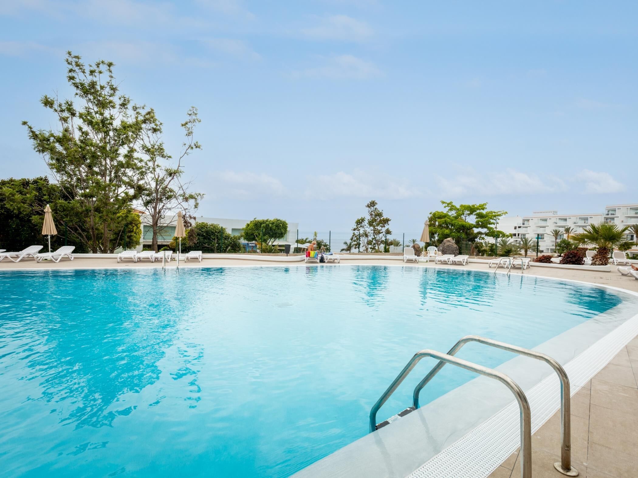 A swimming pool with lounge chairs and umbrellas, surrounded by trees and buildings.