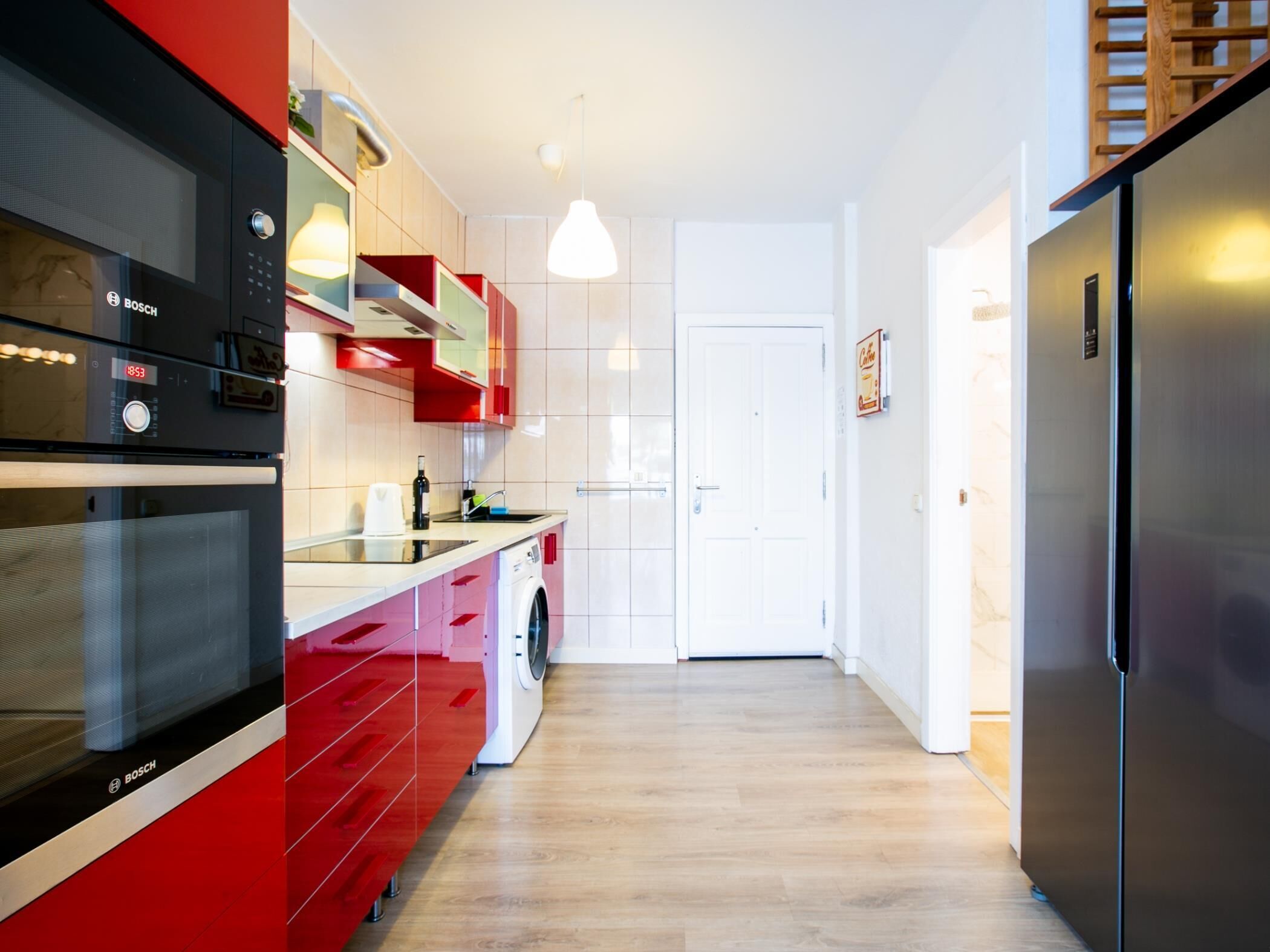 Una cocina moderna con armarios rojos, horno Bosch, lavadora y refrigerador de acero inoxidable.