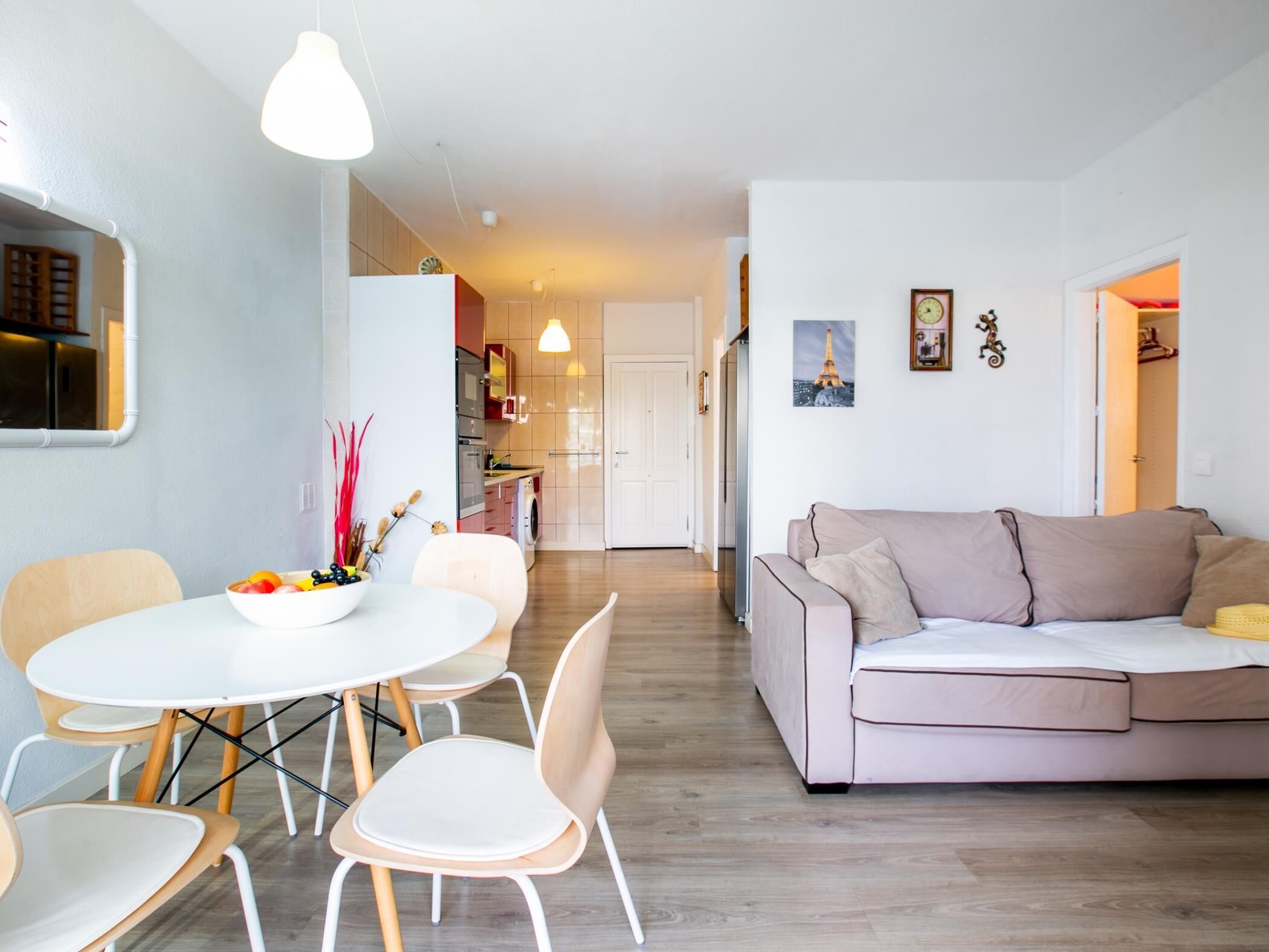 A modern living room with a white sofa, a dining table with chairs, and a kitchen in the background.