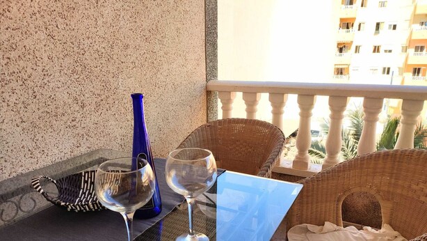 Ein Balkon mit Korbstühlen, einem Glastisch und zwei Weingläsern.
