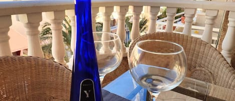 A balcony with wicker furniture, a blue bottle, and two wine glasses.