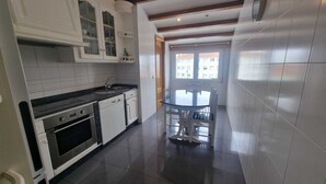 A modern kitchen with white cabinetry, a built-in oven, and a dining area with a glass table and chairs. - Apartamento Sleeps 6 with Garage (Cambados)