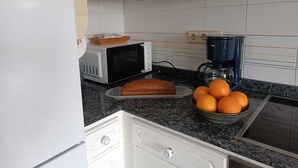 A kitchen with white cabinets, a microwave, a coffee maker, a loaf of bread, and a bowl of oranges on the counter. - Apartamento Sleeps 6 with Garage (Cambados)