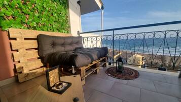A balcony with a wooden bench, a small table with a Buddha statue, and a view of the ocean.