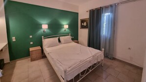 A bedroom with a green wall, a white bed, two bedside lamps, a small wooden nightstand, and a window with curtains.