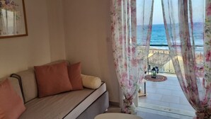 A room with a sofa, floral curtains, and a view of the sea.