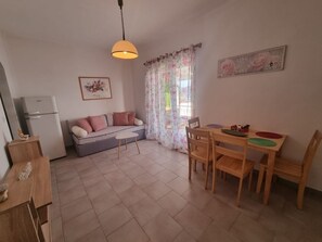 A compact living space with a kitchenette, a sofa, a dining table with chairs, and a window with floral curtains.