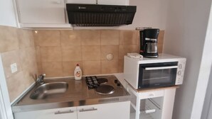 A compact kitchen with a sink, stove, microwave, and a coffee maker.