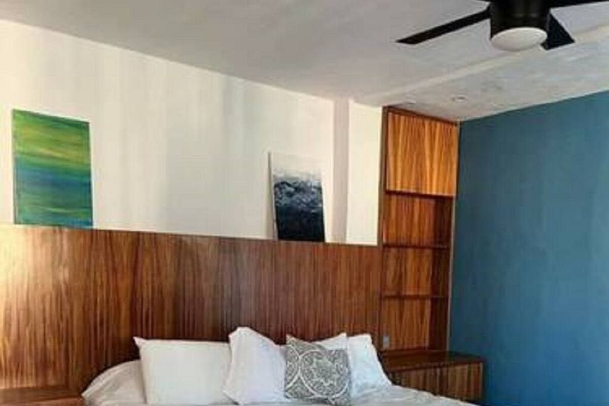 A bedroom with a bed, wooden headboard, ceiling fan, and artwork on the wall.