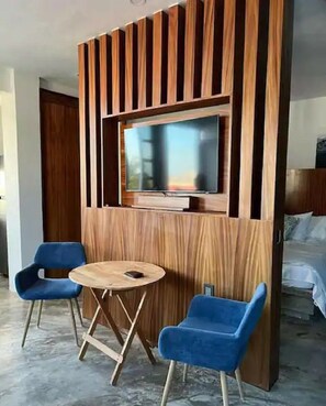 A room with a TV mounted on a wooden panel wall, two blue chairs, and a round wooden table. - Isla Bistro Condos by Lubeck HCollection (Isla Mujeres)