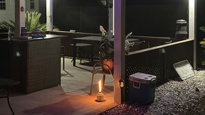 Een buitenpatio met een overdekt zitgedeelte, een tafel en een klok die 4:44 aangeeft.