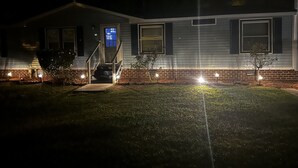 Een huis met een veranda, een trap die naar de deur leidt, en een kleine boom in de voortuin.