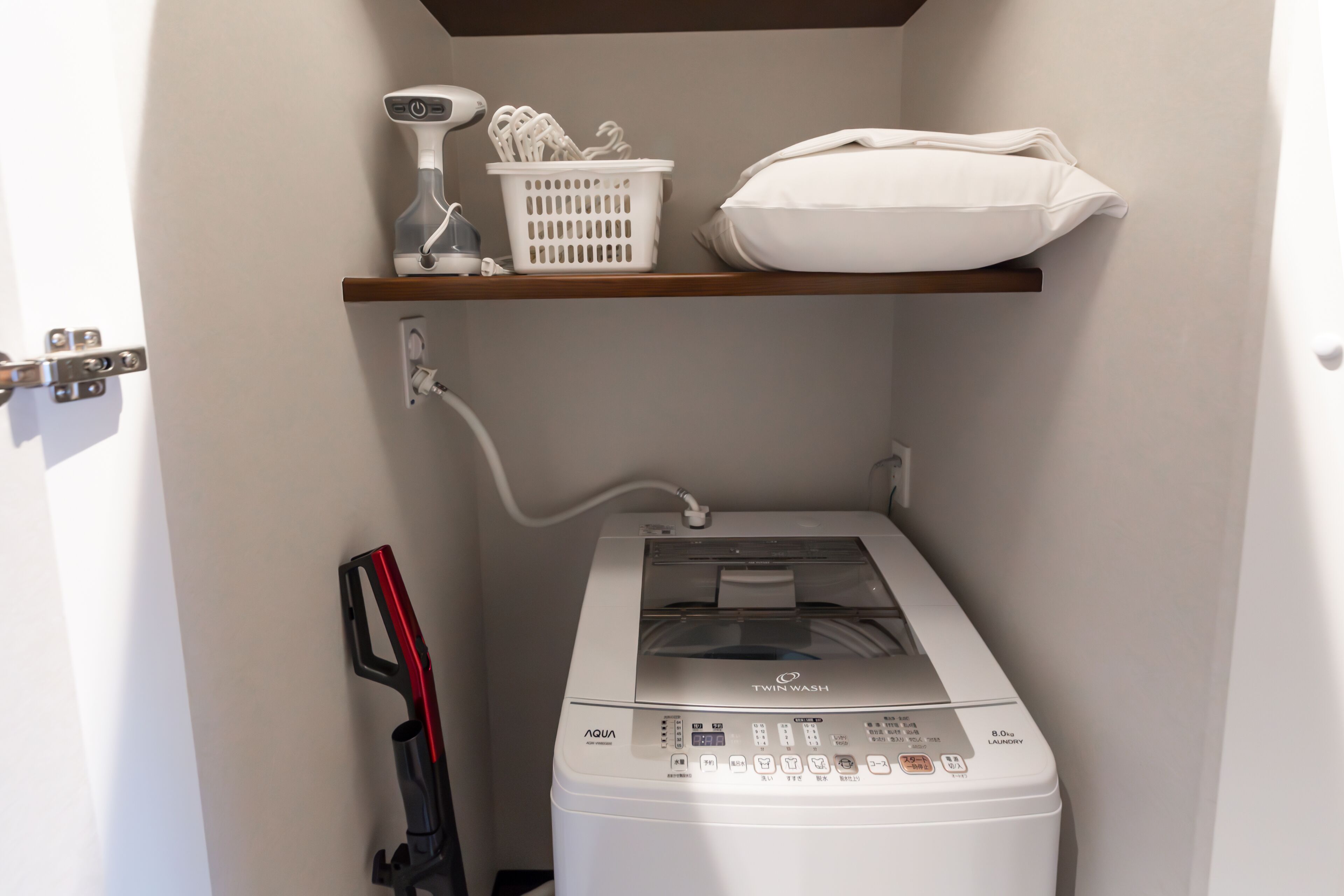 A laundry area with a Twin Wash machine, a basket, and a pillow on a shelf.