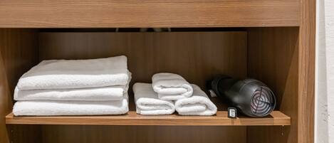 A wooden shelf with neatly folded white towels and a black portable heater.