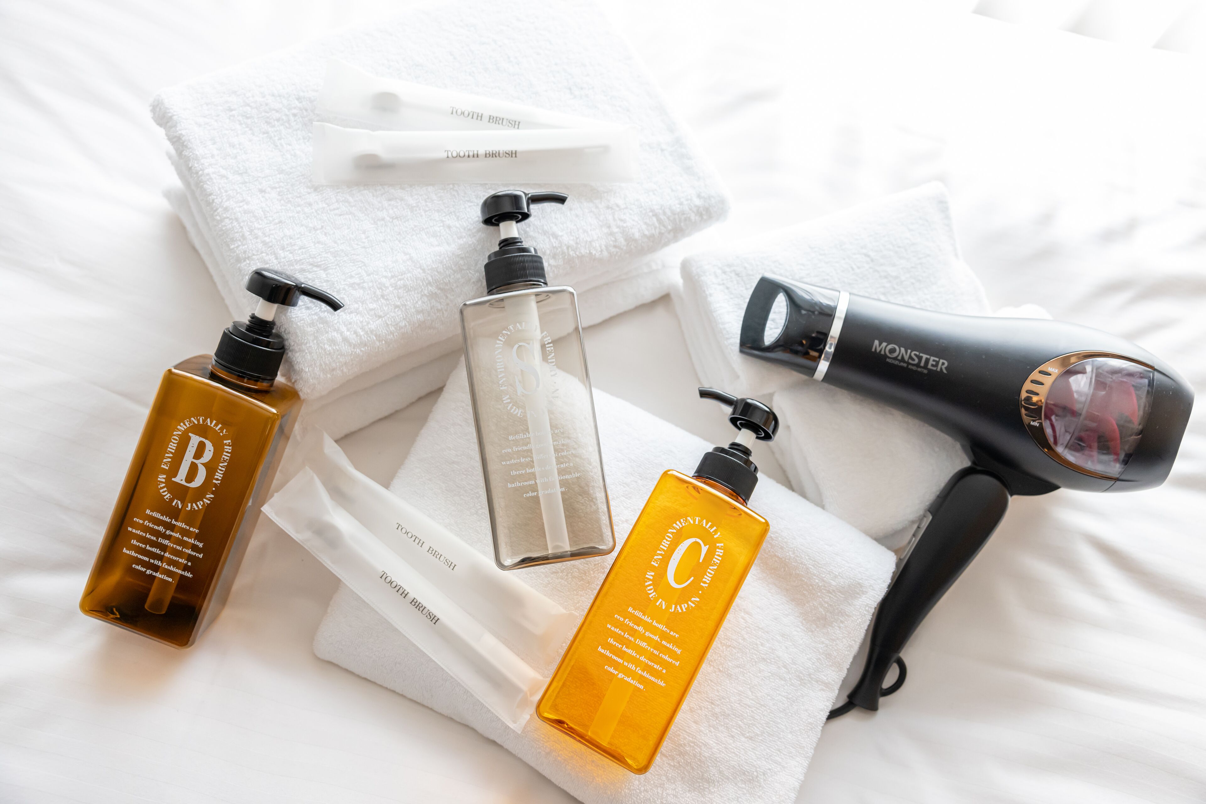A neatly arranged set of toiletries on a white bed with a white towel and a white pillow.